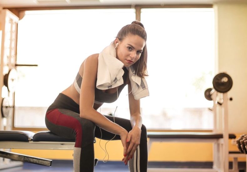 Woman in athletic wear taking a break at the gym with towel and earphones.